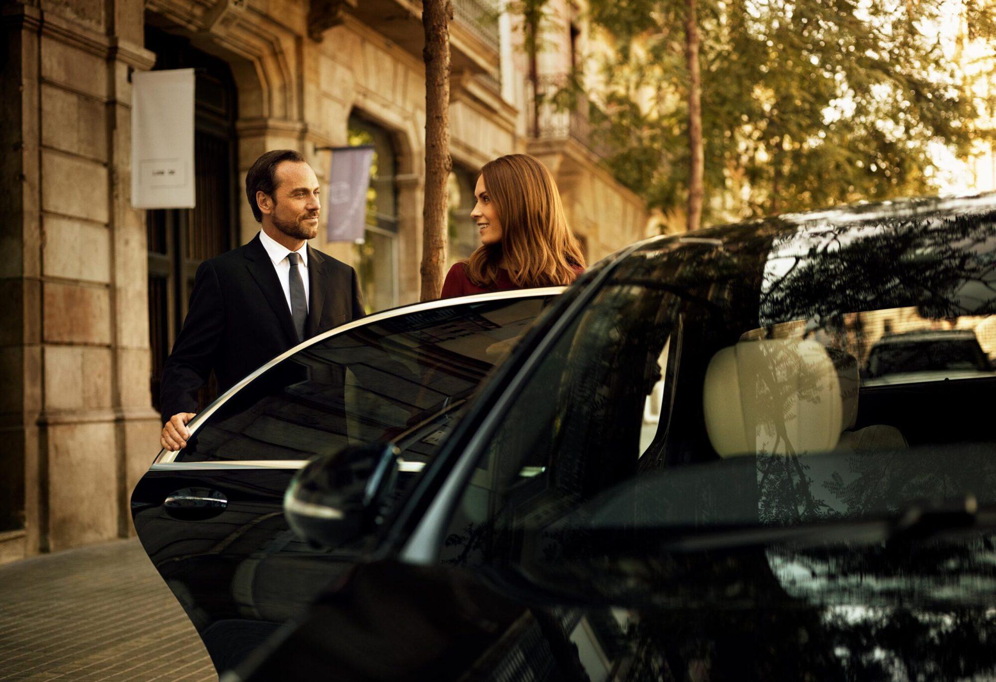 A driver holding the car door open for a passenger